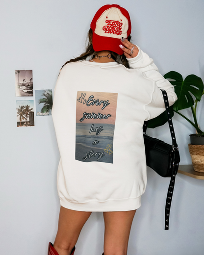 Person wearing a white sweatshirt with a graphic design and a red cap, standing against a light gray wall.