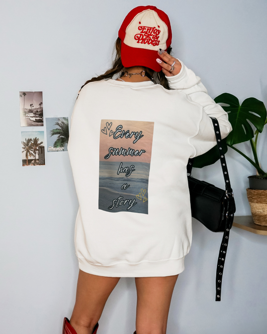 Person wearing a white sweatshirt with a graphic design and a red cap, standing against a light gray wall.