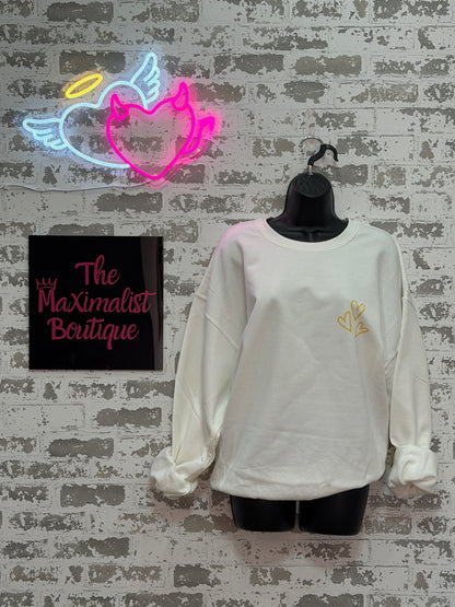 White blouse with gold hearts on a mannequin against a textured wall, with 'The Maximalist Boutique' sign below.