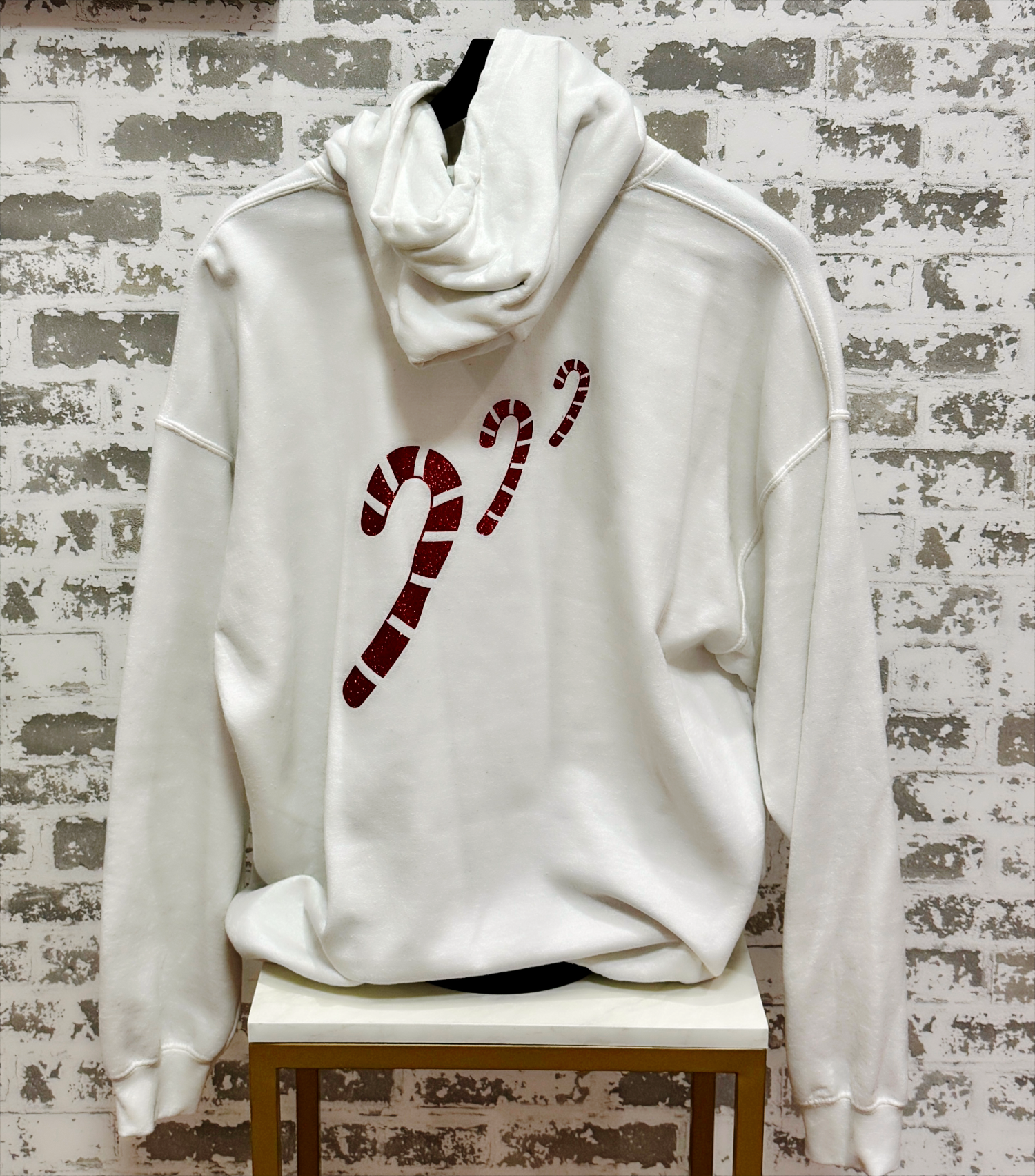 White hoodie with candy cane design on a chair against a textured wall.