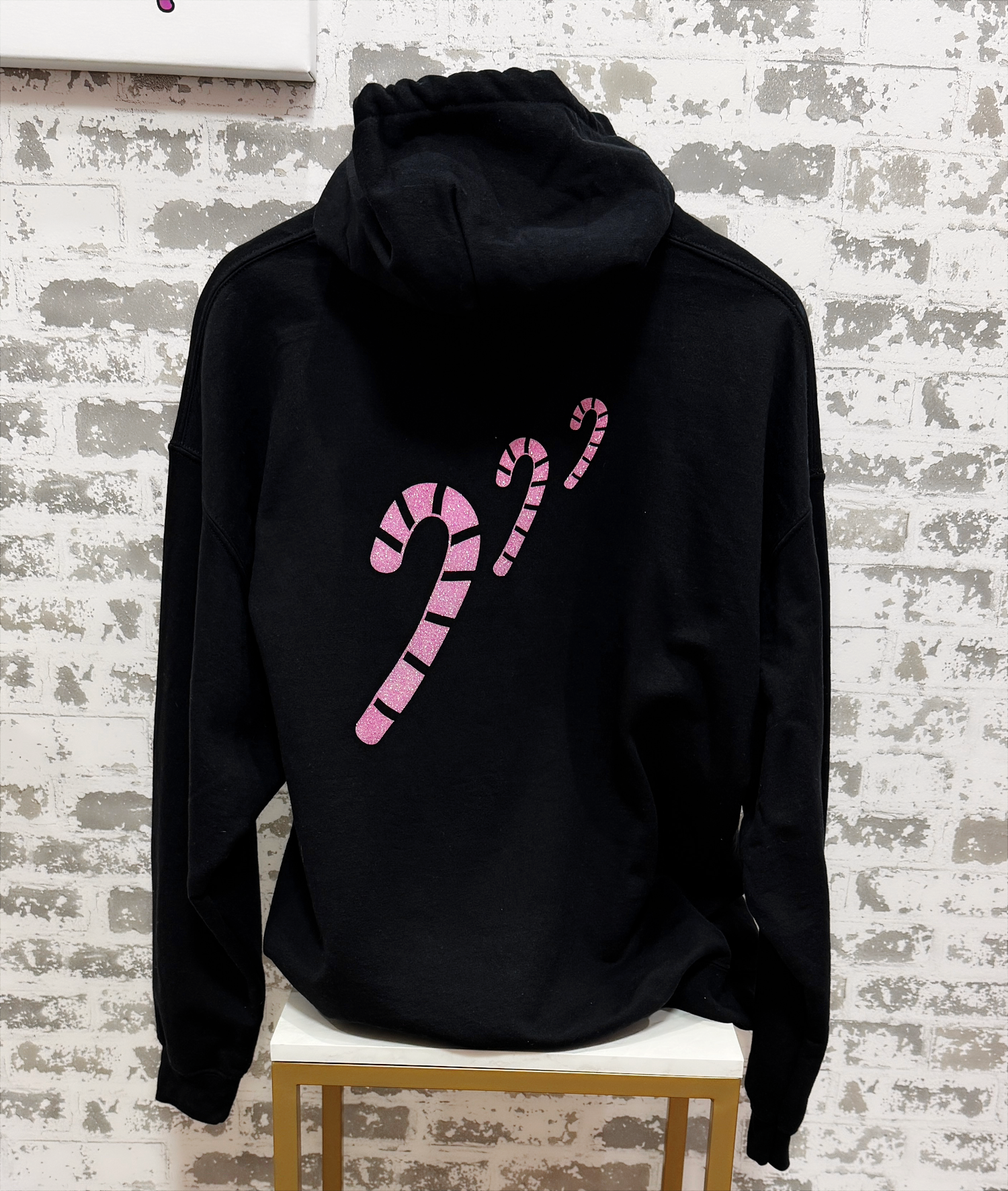Black hoodie with pink candy cane design on a textured white wall