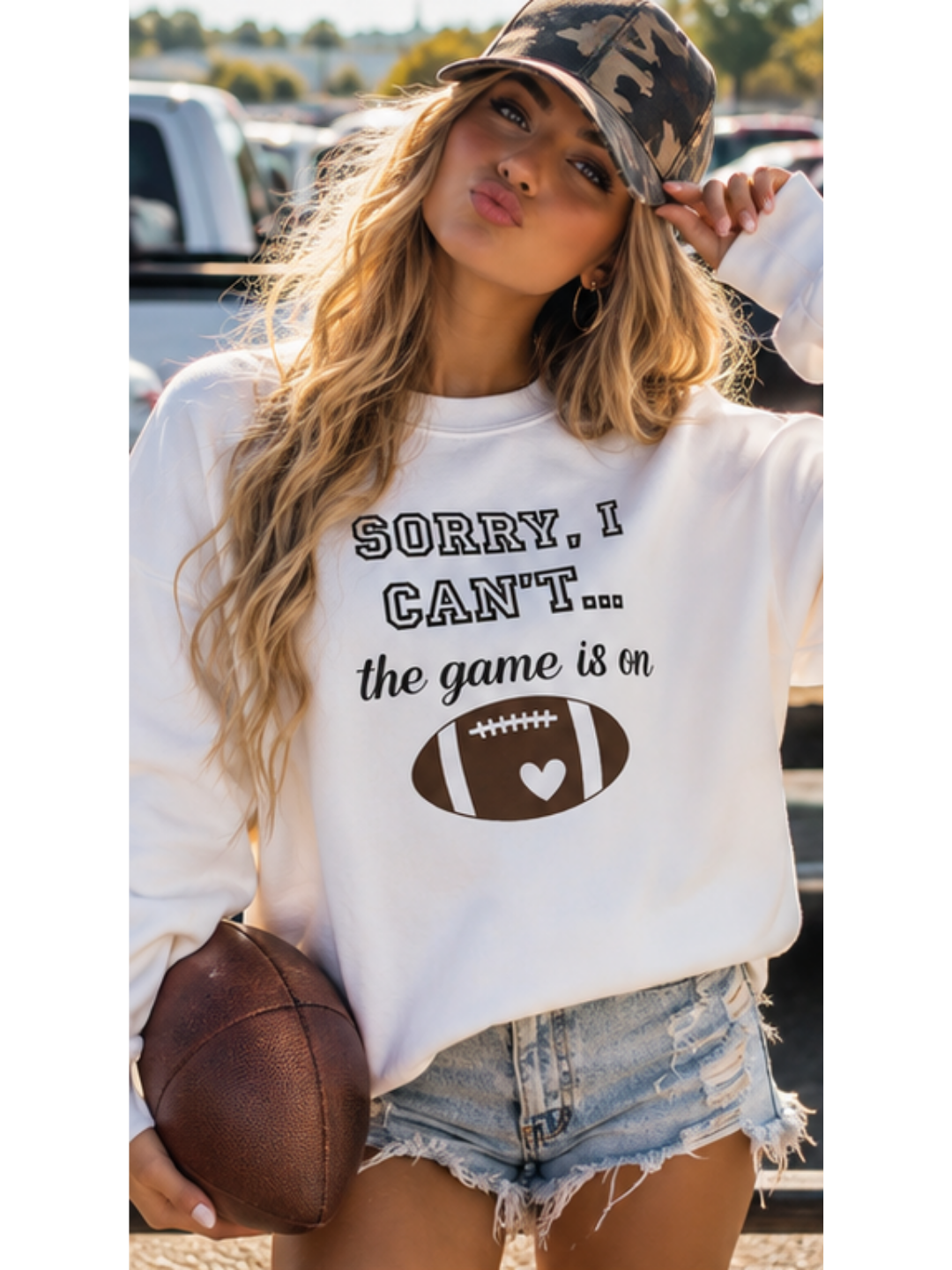 Woman wearing a sweatshirt with a football graphic and text, holding a football outside