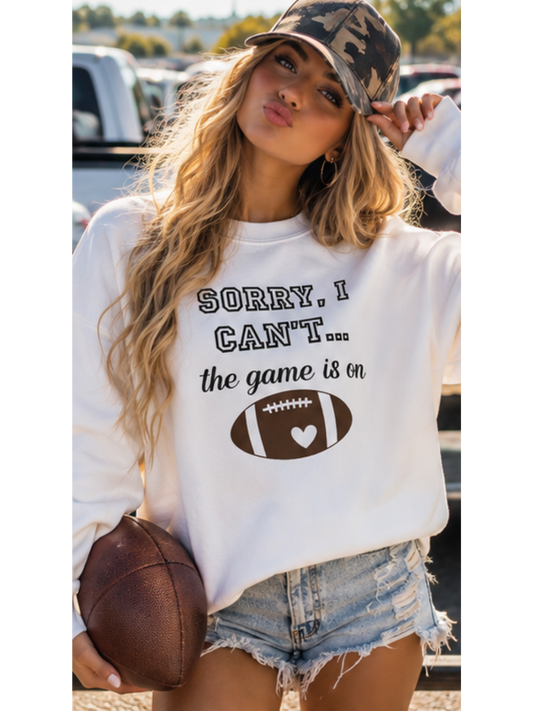 Woman wearing a sweatshirt with a football graphic and text, holding a football outside