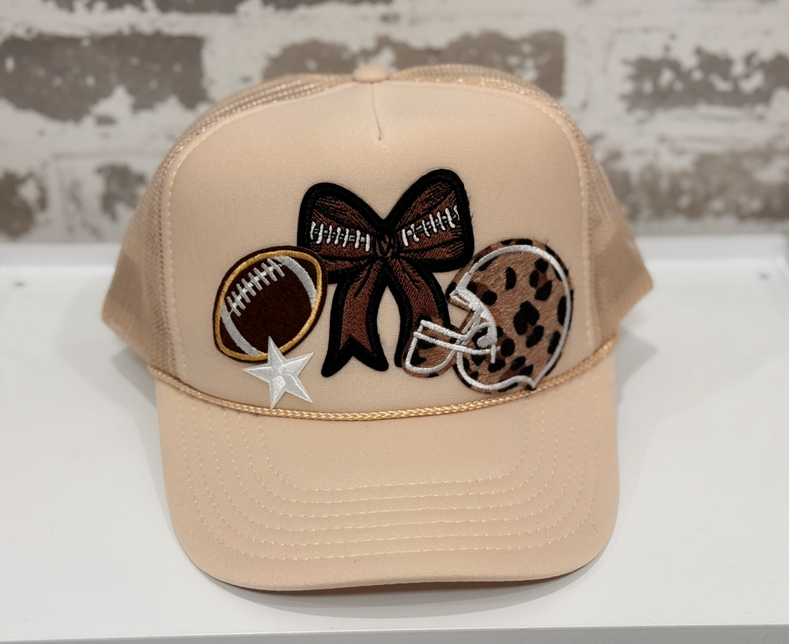 Beige cap with decorative patches including a bow, football, helmet, and star on a white surface.