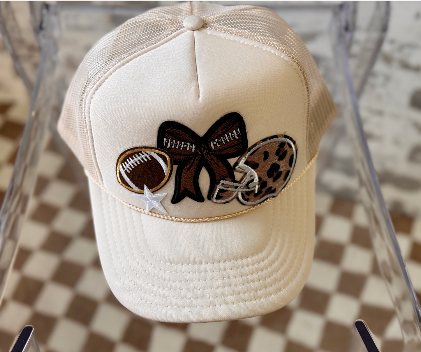 Beige cap with decorative bow featuring football and leopard print elements on a checkered background.