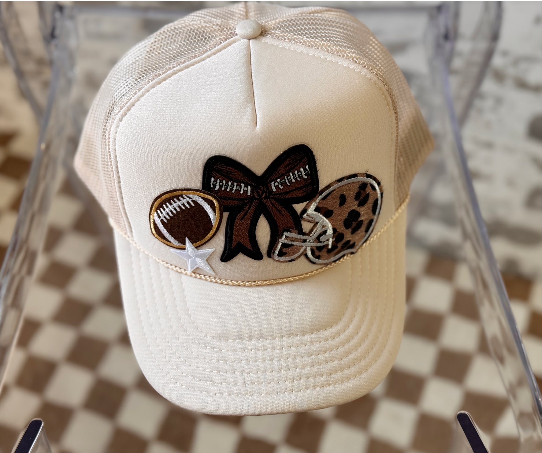 Beige cap with decorative bow featuring football and leopard print elements on a checkered background.