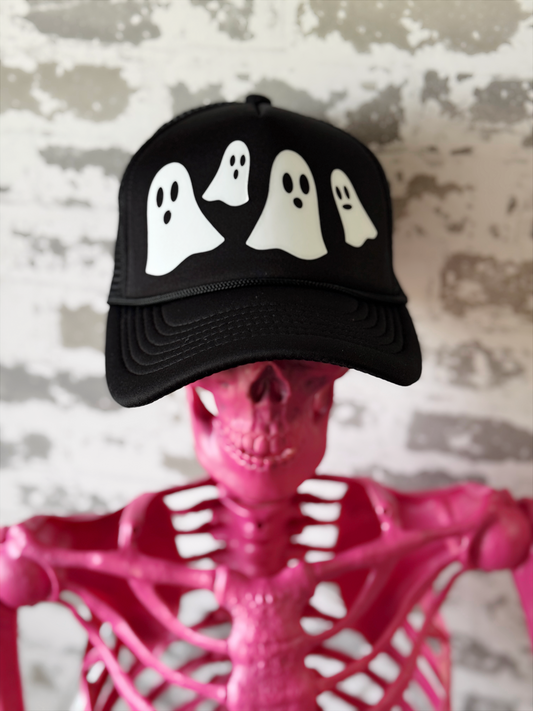 Black cap with white ghost designs on a pink skeleton against a textured wall.
