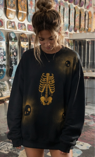 A woman wearing a black crewneck sweatshirt with a gold skeleton rib cage graphic and skull motifs, standing in a shop with skateboards on the wall behind her.