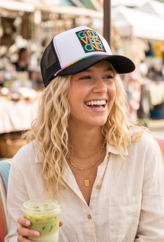 Woman wearing a colorful cap and holding a drink, smiling outdoors.