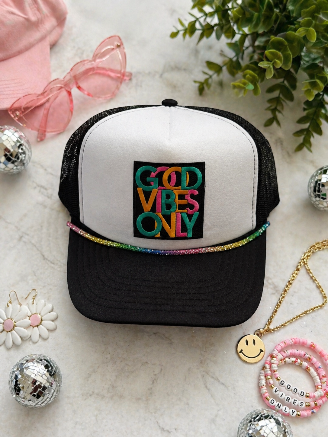 Trucker hat with 'Good Vibes Only' text on a marble surface with decorative items.
