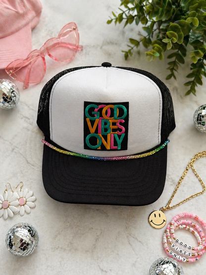 Trucker hat with 'Good Vibes Only' text on a marble surface with decorative items.