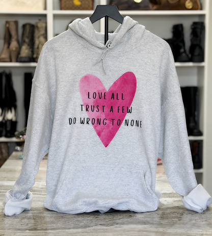 Gray hoodie with pink heart and text on a wooden surface with shelves in the background