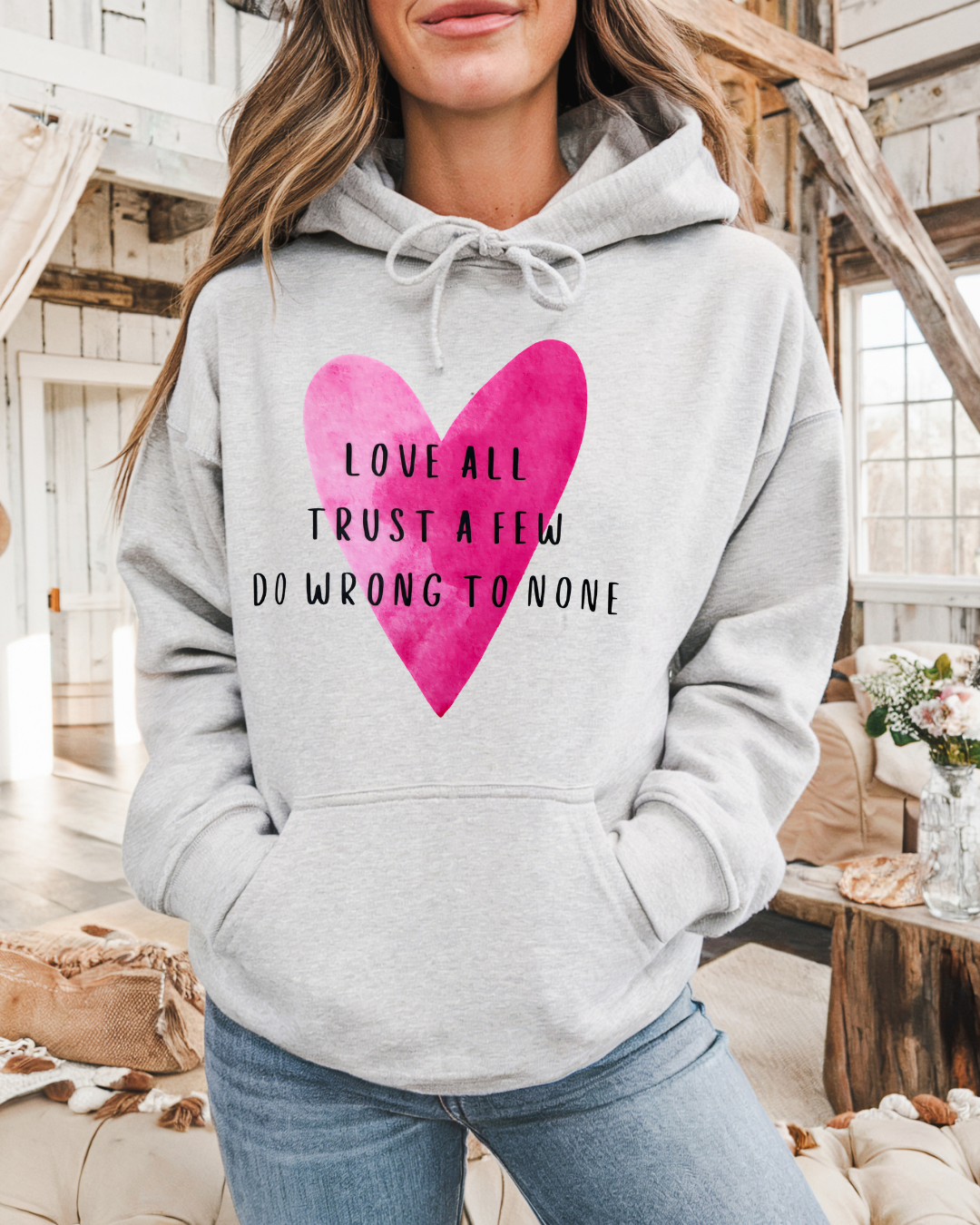 Person wearing a gray hoodie with a pink heart and text in a rustic indoor setting