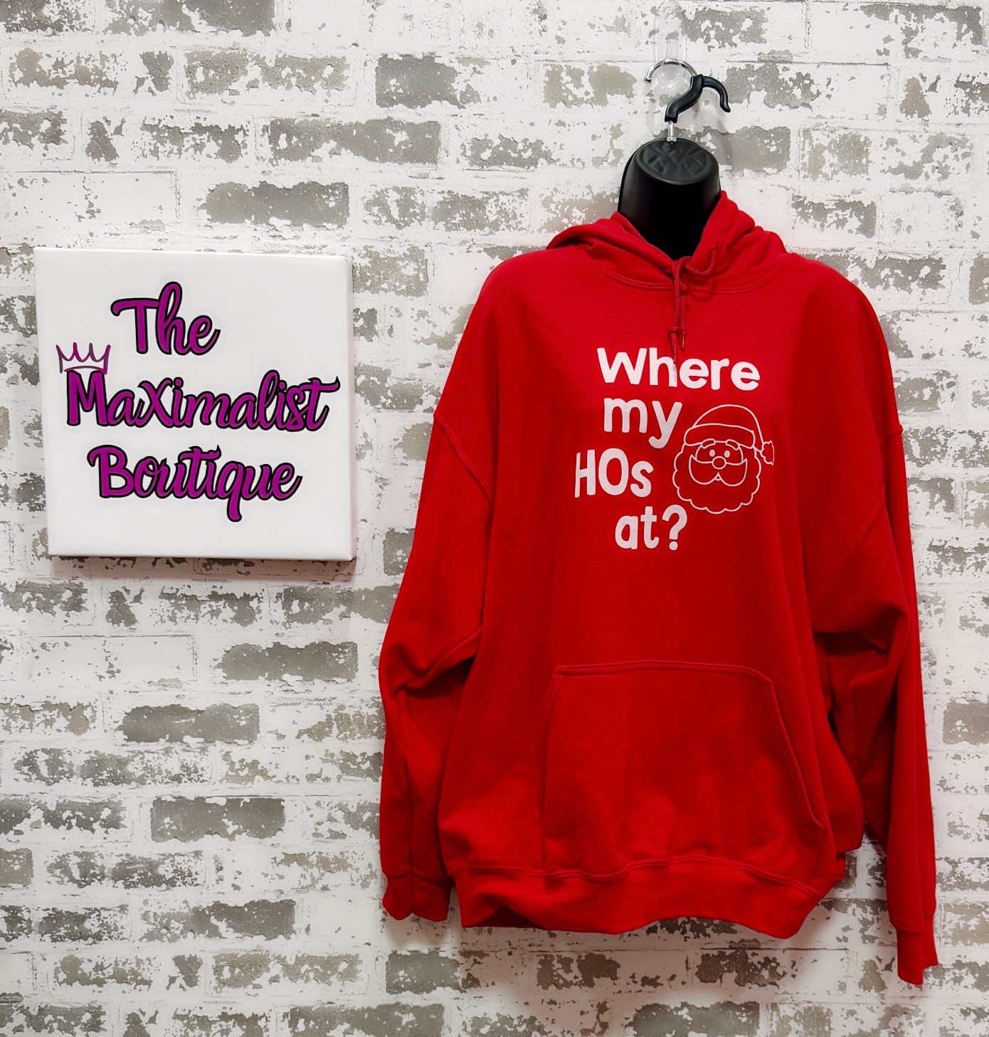 Red hoodie with text on a textured wall, next to a sign for 'The Maximalist Boutique'.