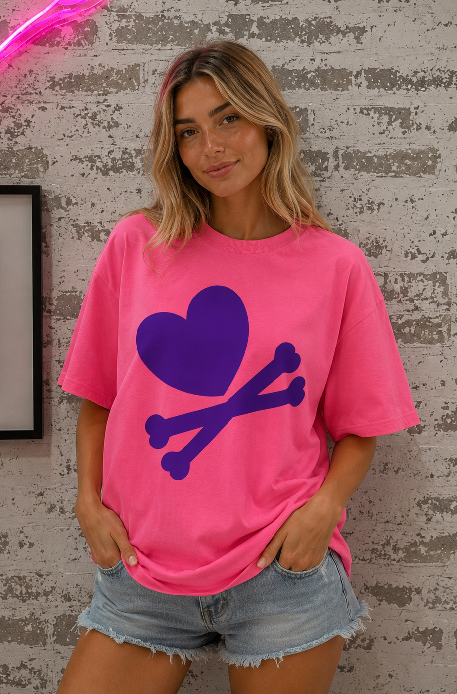 Woman wearing a pink t-shirt with a purple heart and bones design against a textured wall.