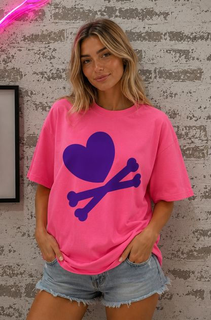 Woman wearing a pink t-shirt with a purple heart and bones design against a textured wall.