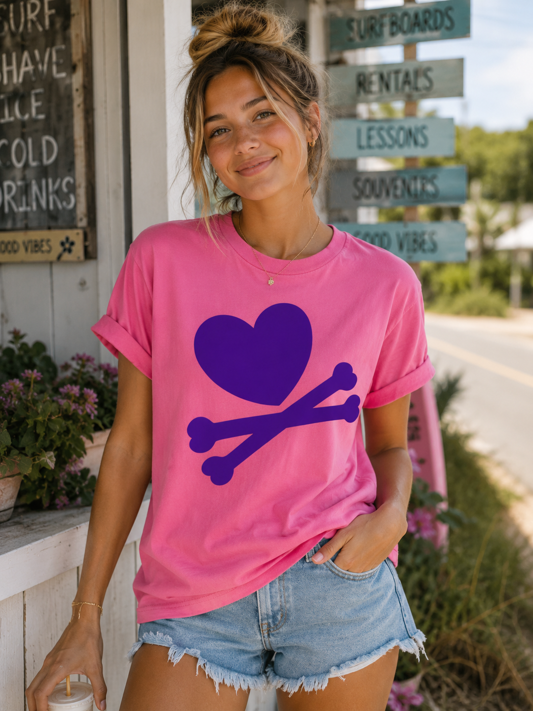 Woman wearing a pink t-shirt with a purple heart and bones design, standing outdoors.