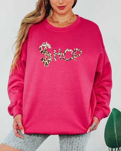 Person wearing a pink sweatshirt with 'SHOP' in leopard print letters on a plain background