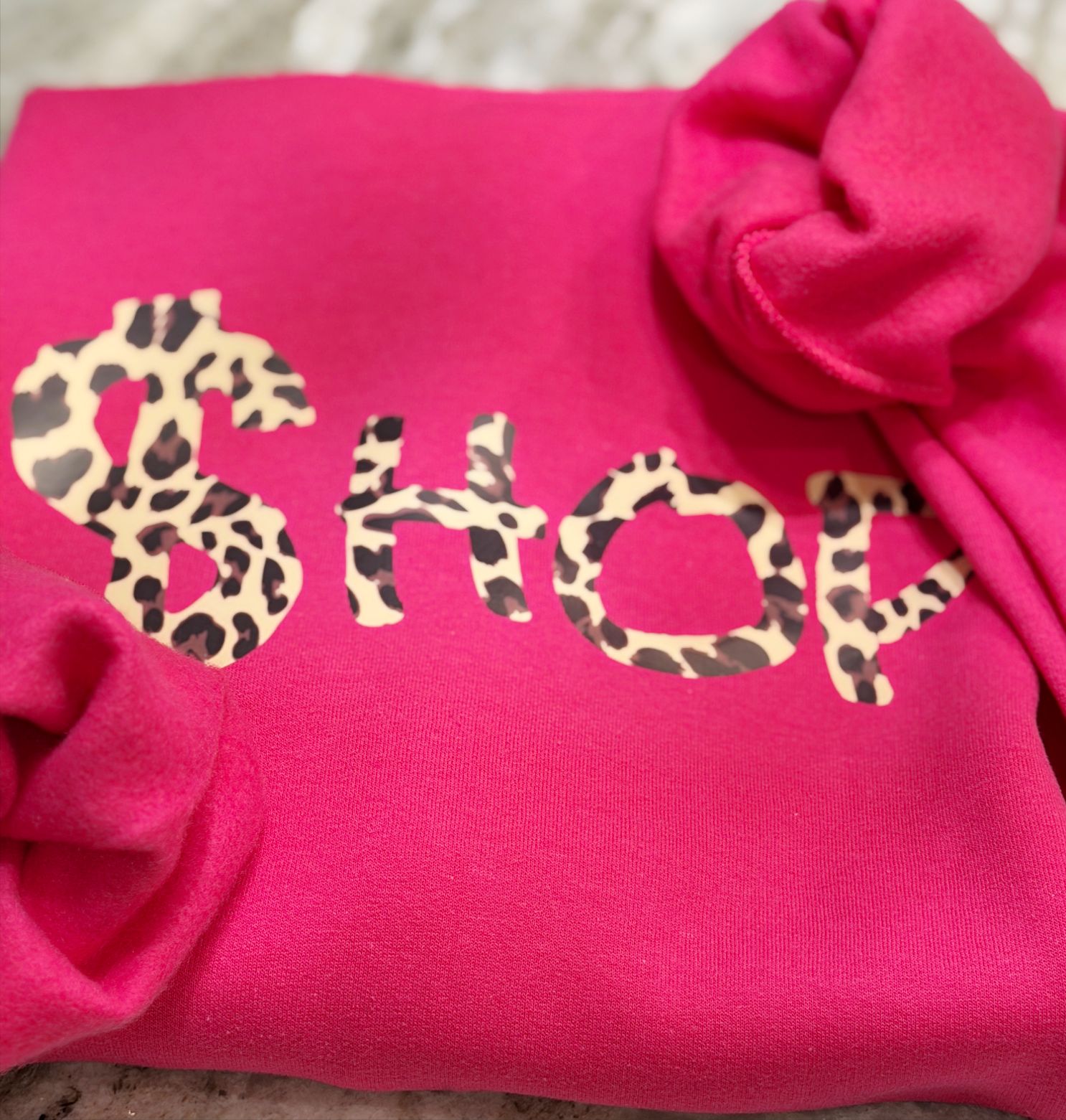 Pink sweatshirt with 'SHOP' in leopard print letters on a textured surface