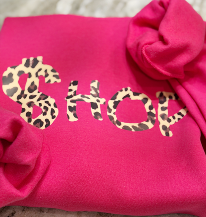 Pink sweatshirt with 'SHOP' in leopard print letters on a textured surface