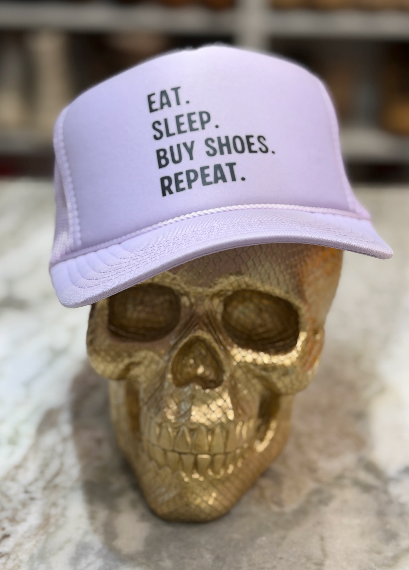 Light purple cap with 'Eat. Sleep. Buy Shoes. Repeat.' text on a gold skull.