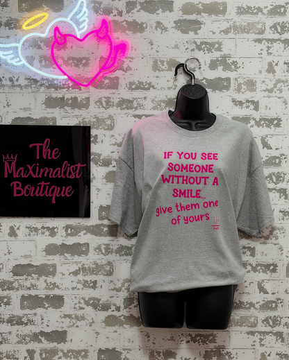 Gray t-shirt with pink text on a mannequin against a brick wall with neon signs.