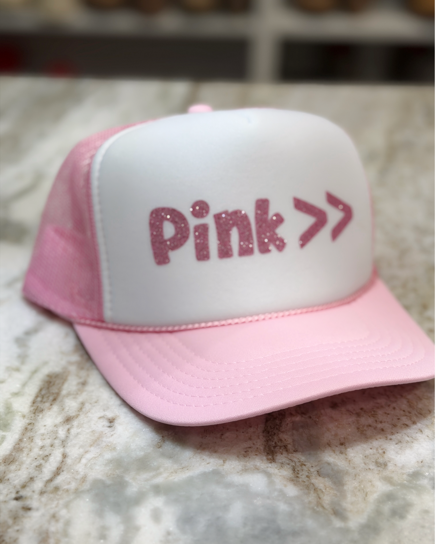 Pink and white cap with 'Pink >>' text on a marble surface