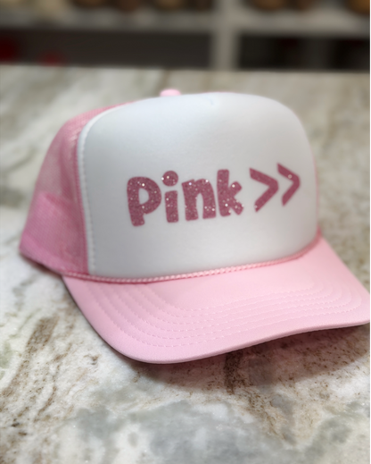 Pink and white cap with 'Pink >>' text on a marble surface