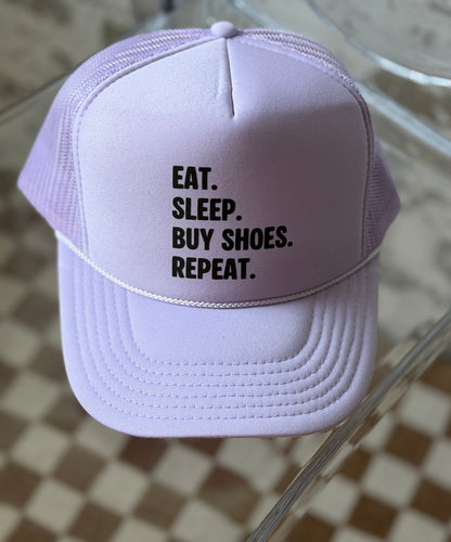 Purple cap with text 'EAT. SLEEP. BUY SHOES. REPEAT.' on a checkered floor background