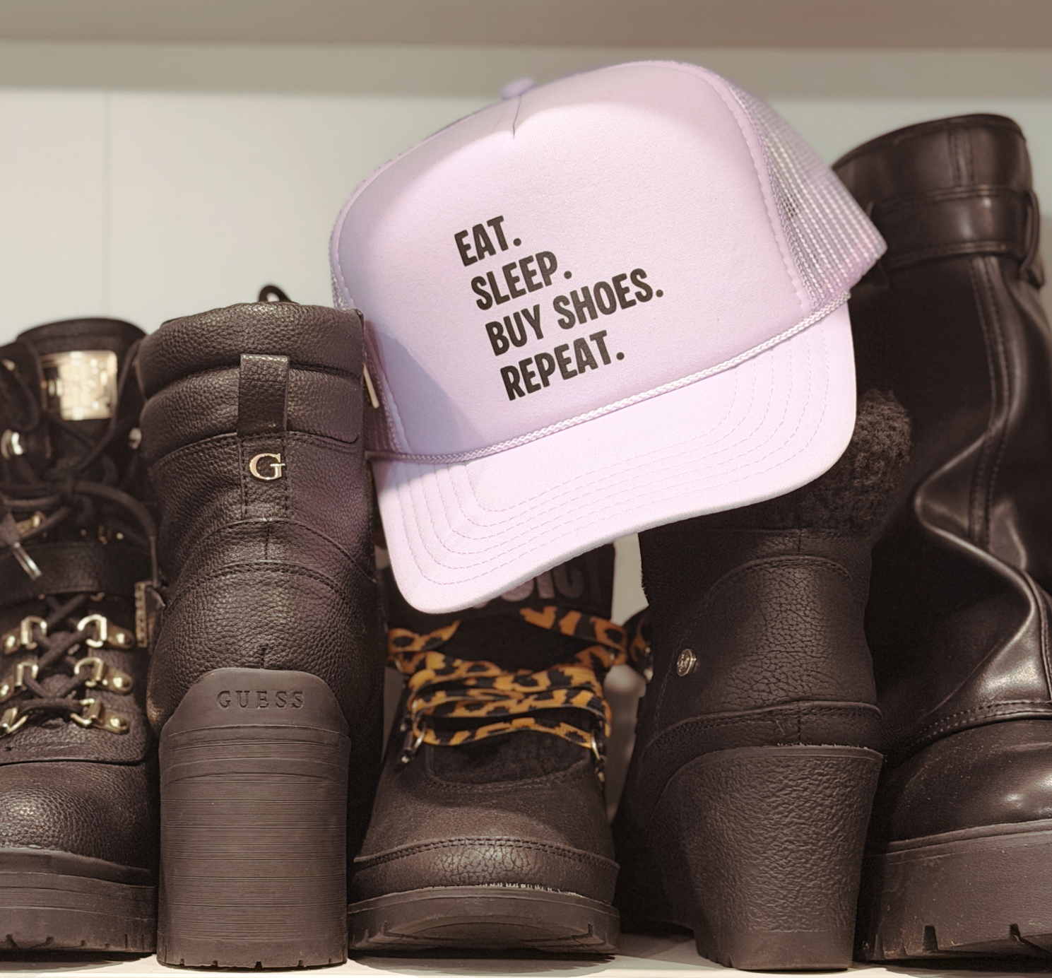 Lavender cap with 'Eat. Sleep. Buy Shoes. Repeat.' text on a pile of shoes.