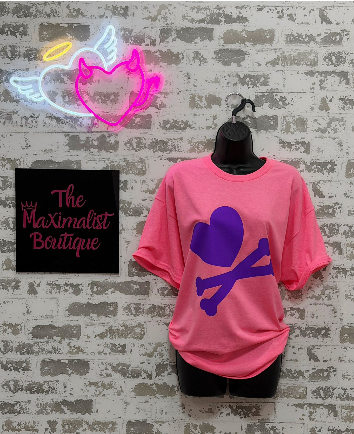 Pink t-shirt with purple graphic design on a mannequin against a textured wall with 'The Maximalist Boutique' sign.
