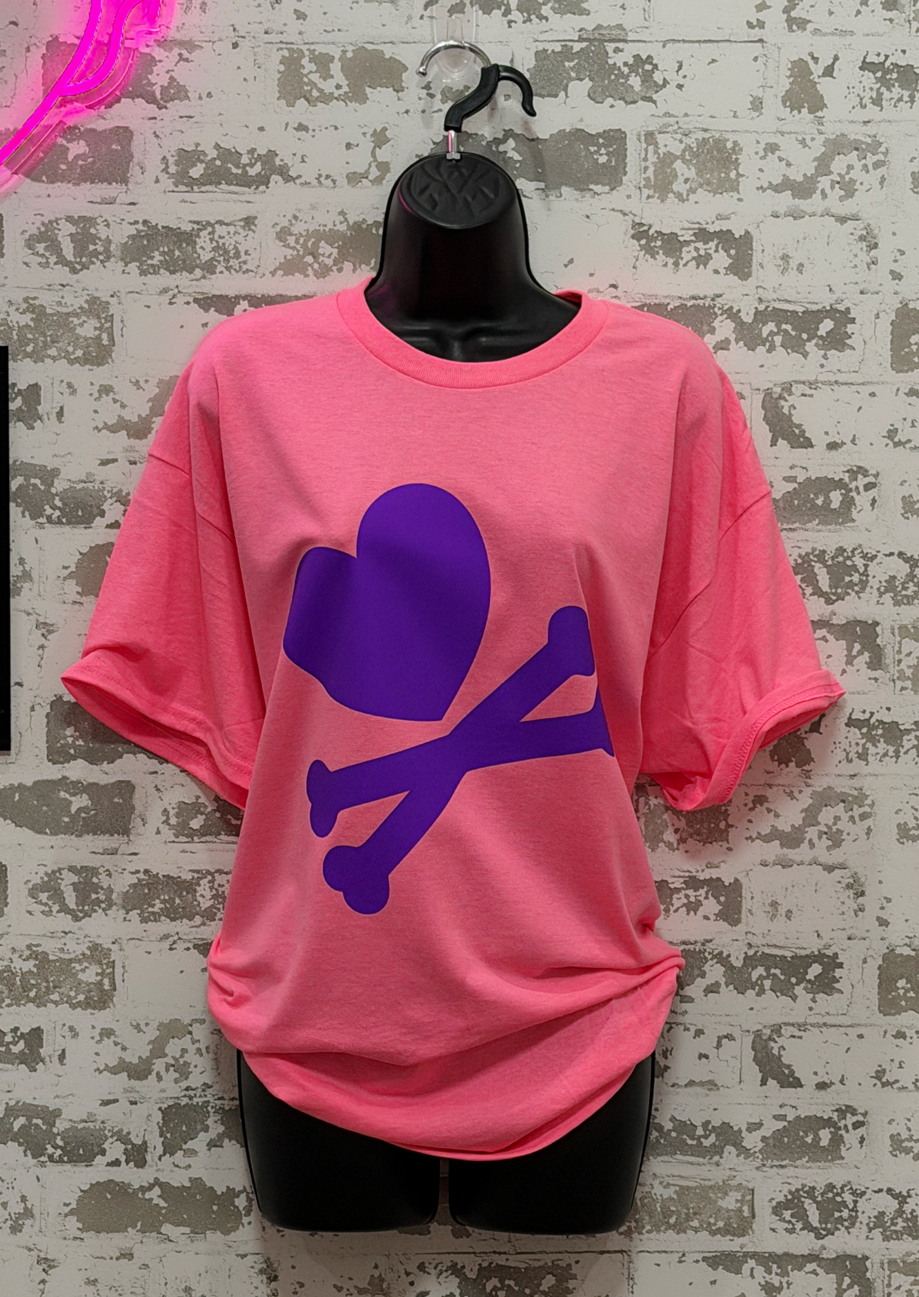 Pink t-shirt with purple graphic on a mannequin against a textured wall background