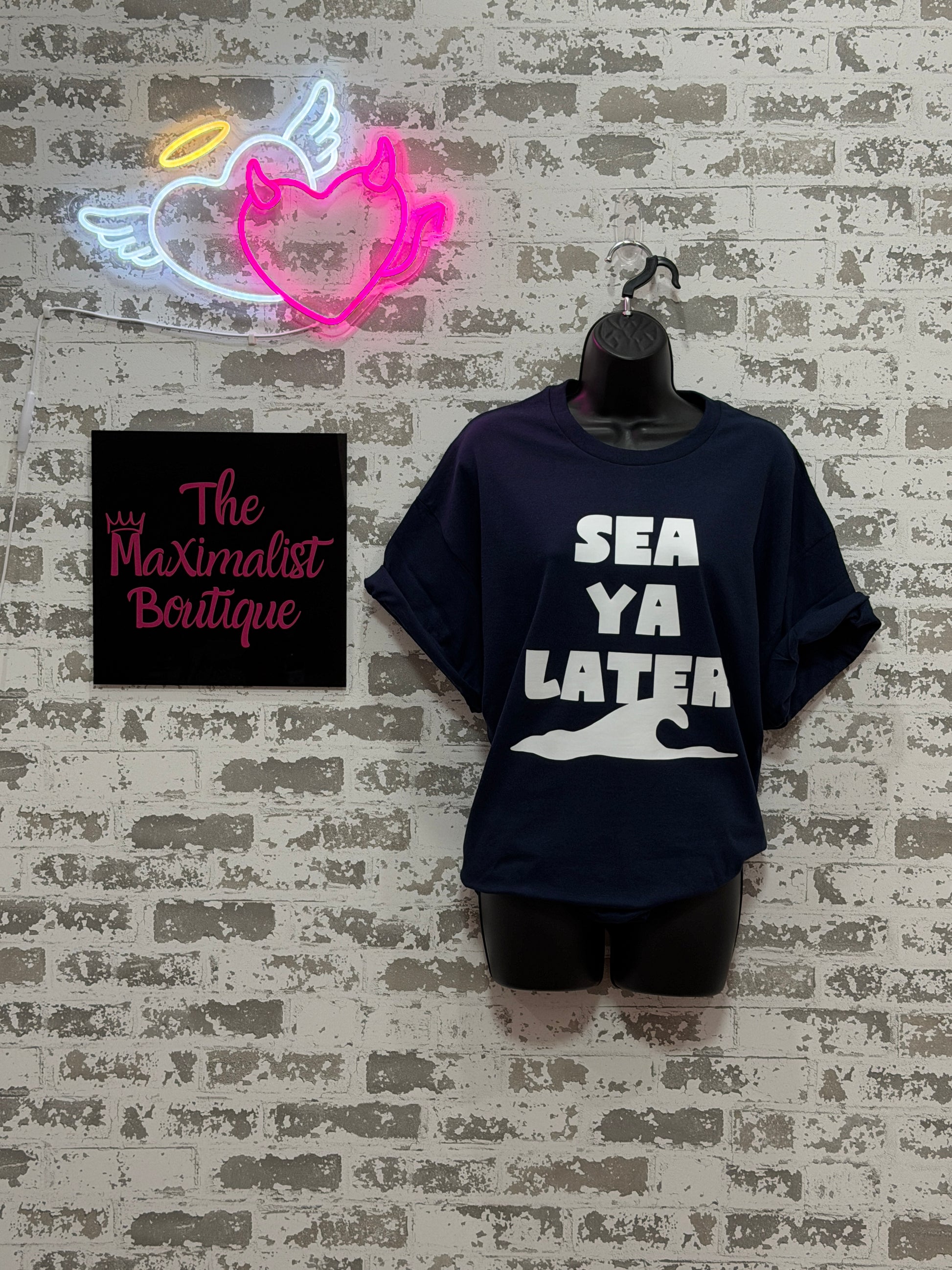Black t-shirt with white text on a textured surface, next to a neon sign and a card with text.