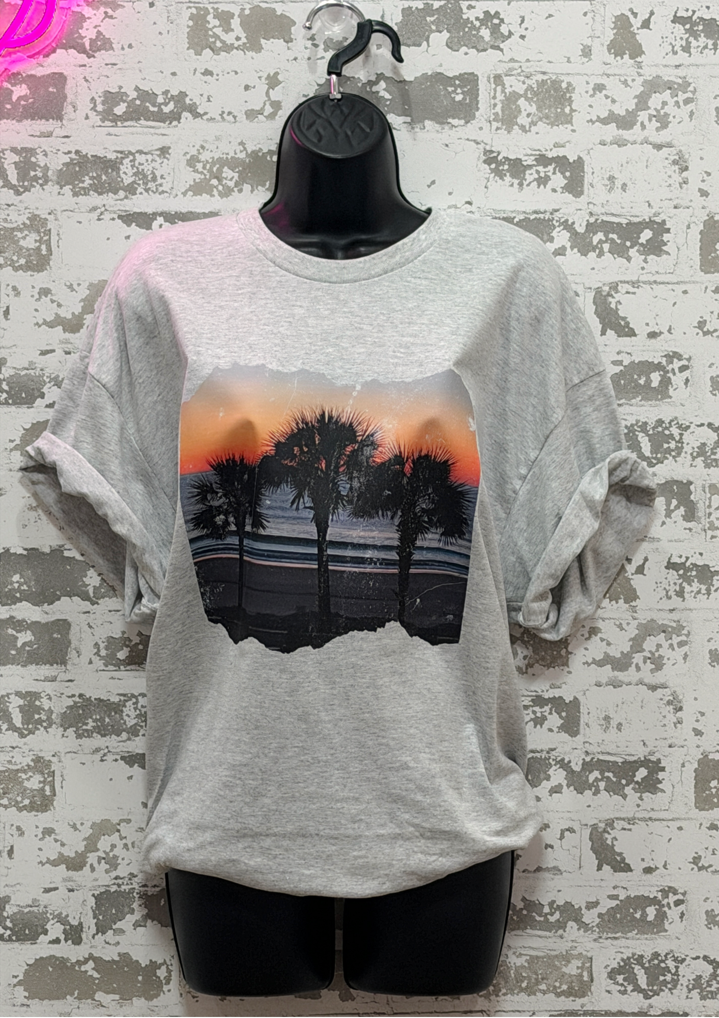 Gray t-shirt with a palm tree design on a textured wall background