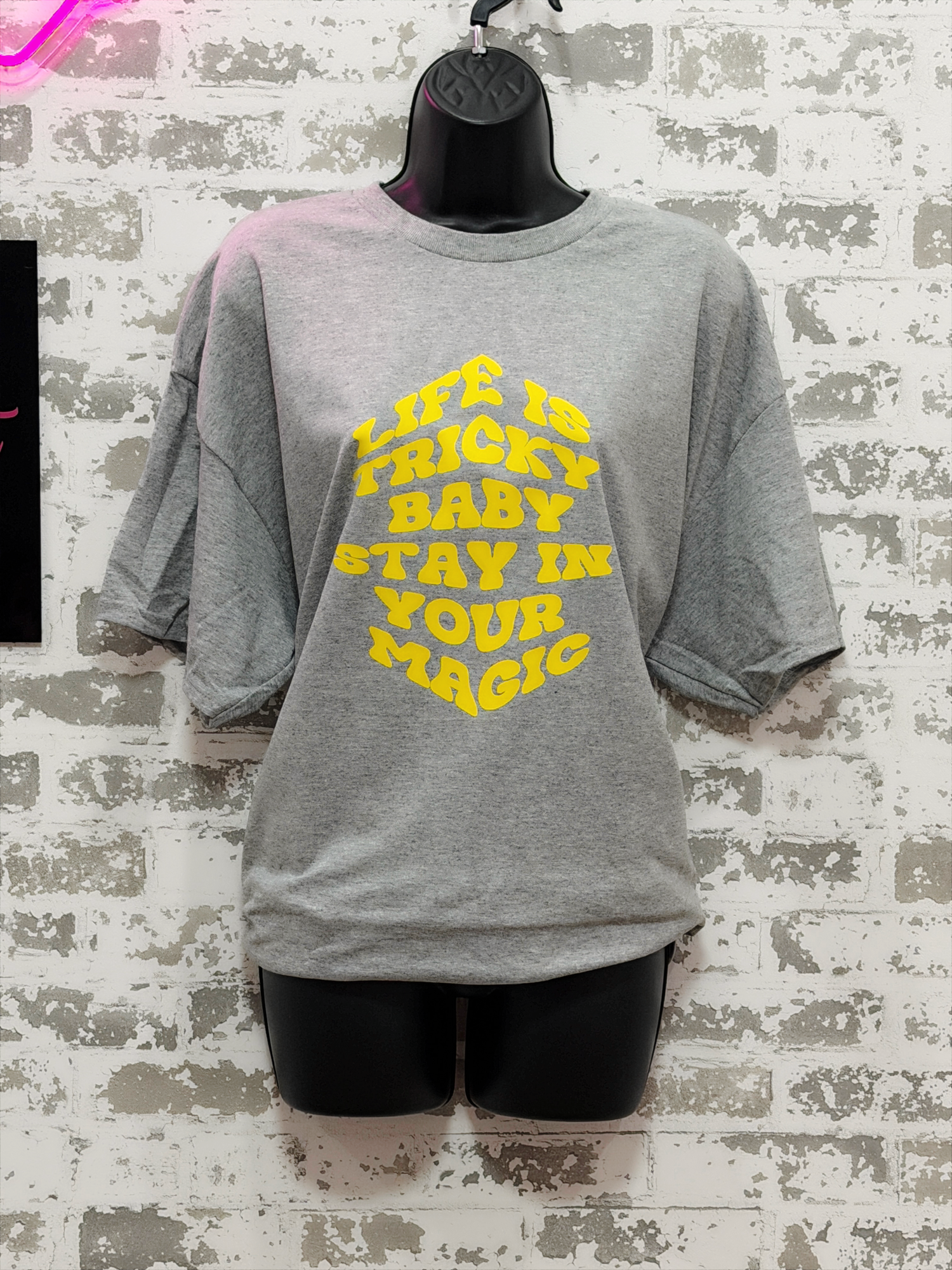 Gray t-shirt with yellow text on a textured wall background