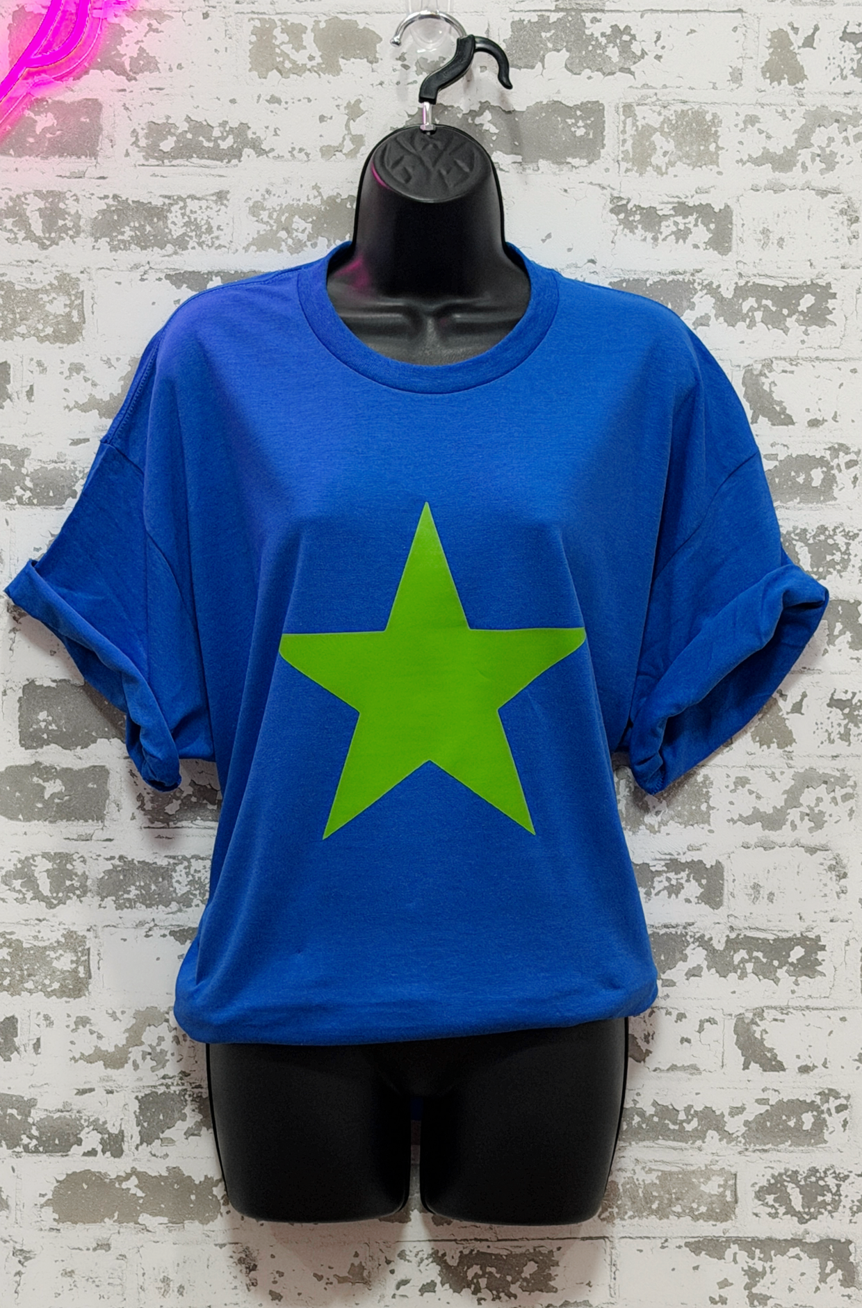 Blue t-shirt with a green star on a mannequin against a textured wall background