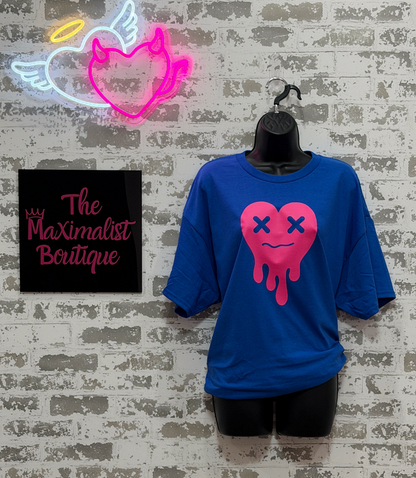 Blue t-shirt with pink heart design on a mannequin against a textured wall with neon sign and 'The Maximalist Boutique' sign.