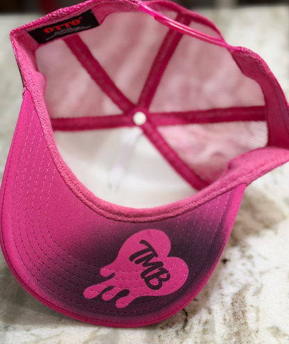 A pink snapback cap with a gradient fade from bright pink to dark purple, featuring a pink heart-shaped graphic with the letters 'TMB' on the brim. The inside of the cap shows a pink mesh back and a black brand label reading 'OTTO'.