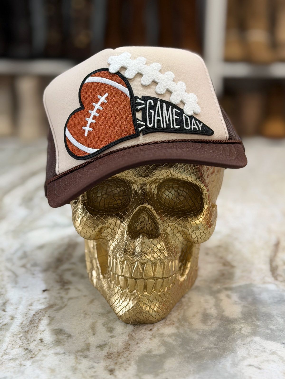 Game Day Heart Trucker Hat featuring a cream front, chocolate brown bill, and a football-heart patch with dimensional lace and GAME DAY text.