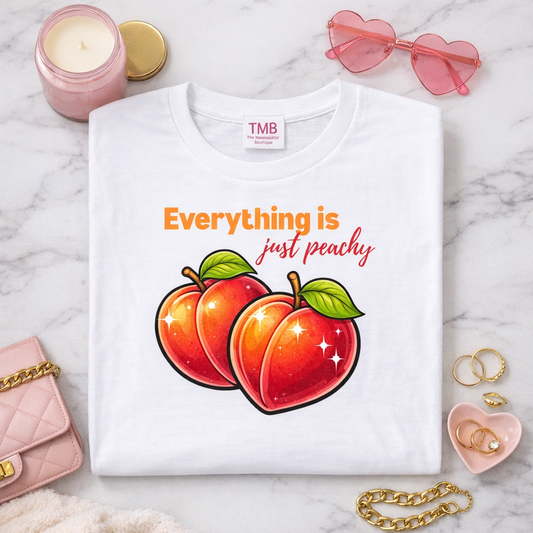 White t-shirt with peach design and text on a marble surface with accessories.