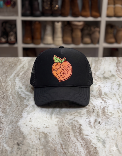 Black cap with peach logo on a marble surface with boots in the background