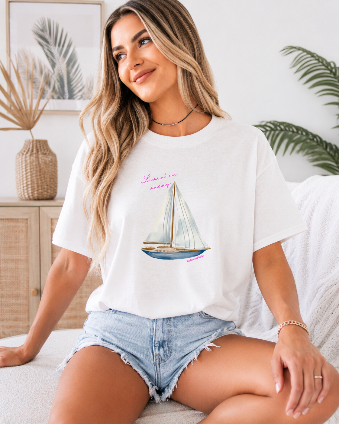 Woman wearing a white t-shirt with a sailboat graphic and text, sitting on a couch.