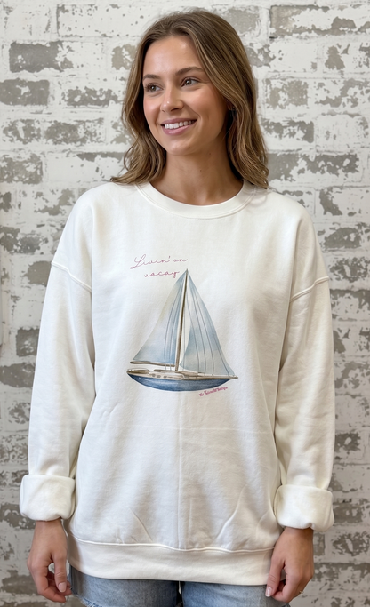 Woman wearing a cream sweatshirt with a sailboat design against a textured wall.