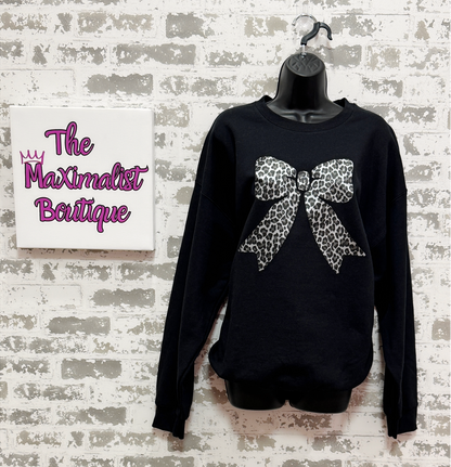 Black sweatshirt with a leopard print bow on a mannequin against a textured wall with 'The Maximalist Boutique' sign.