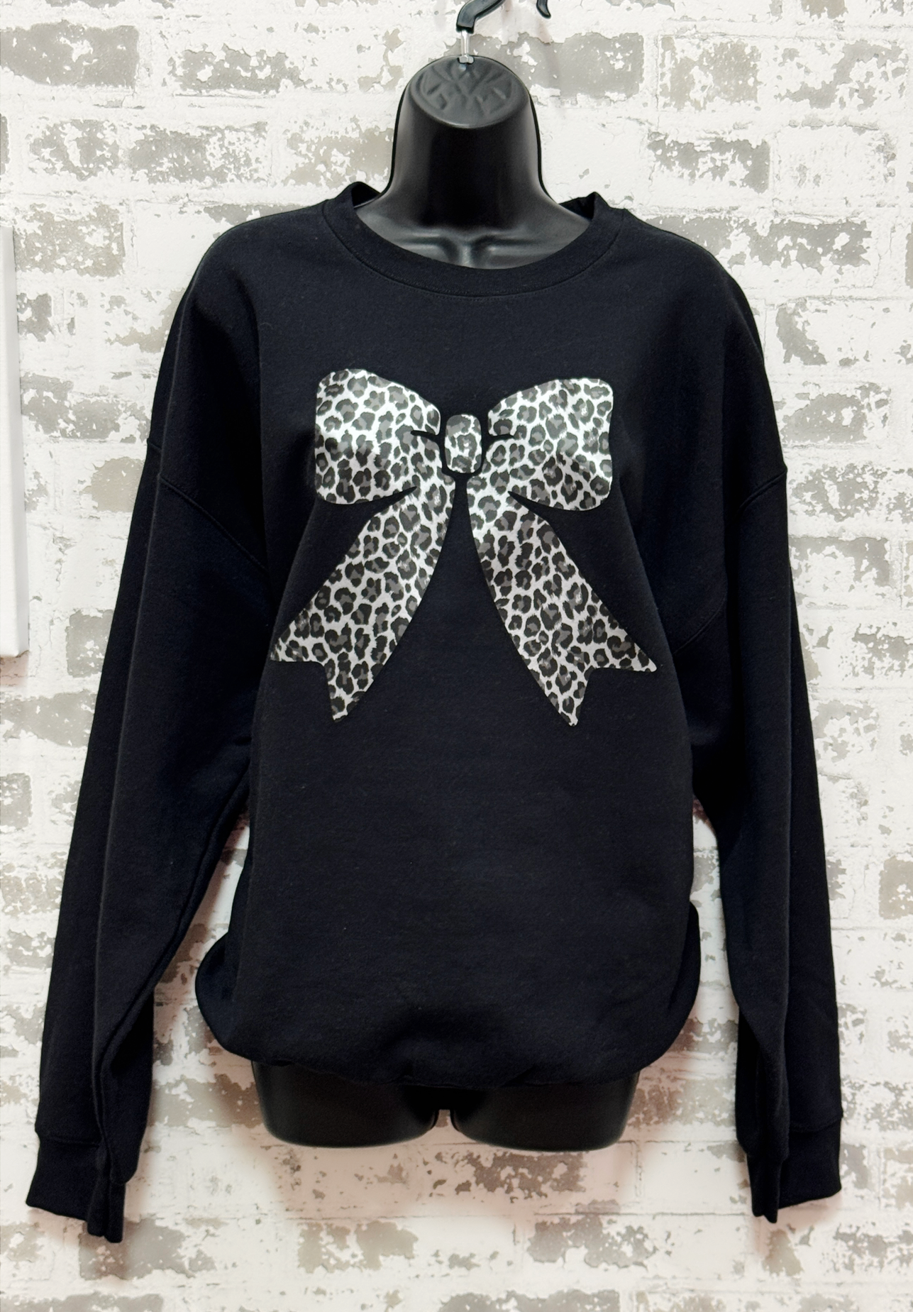 Black sweater with a large leopard print bow on a textured white background