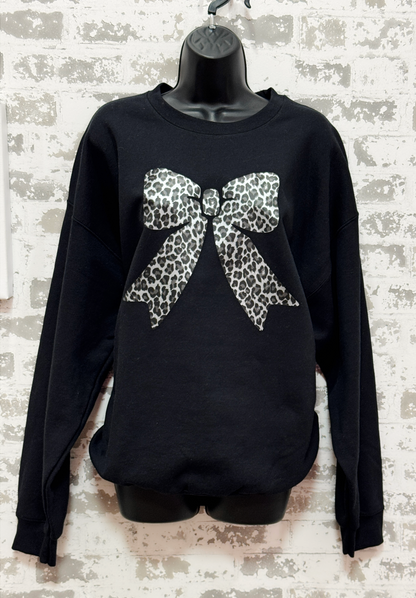 Black sweater with a large leopard print bow on a textured white background