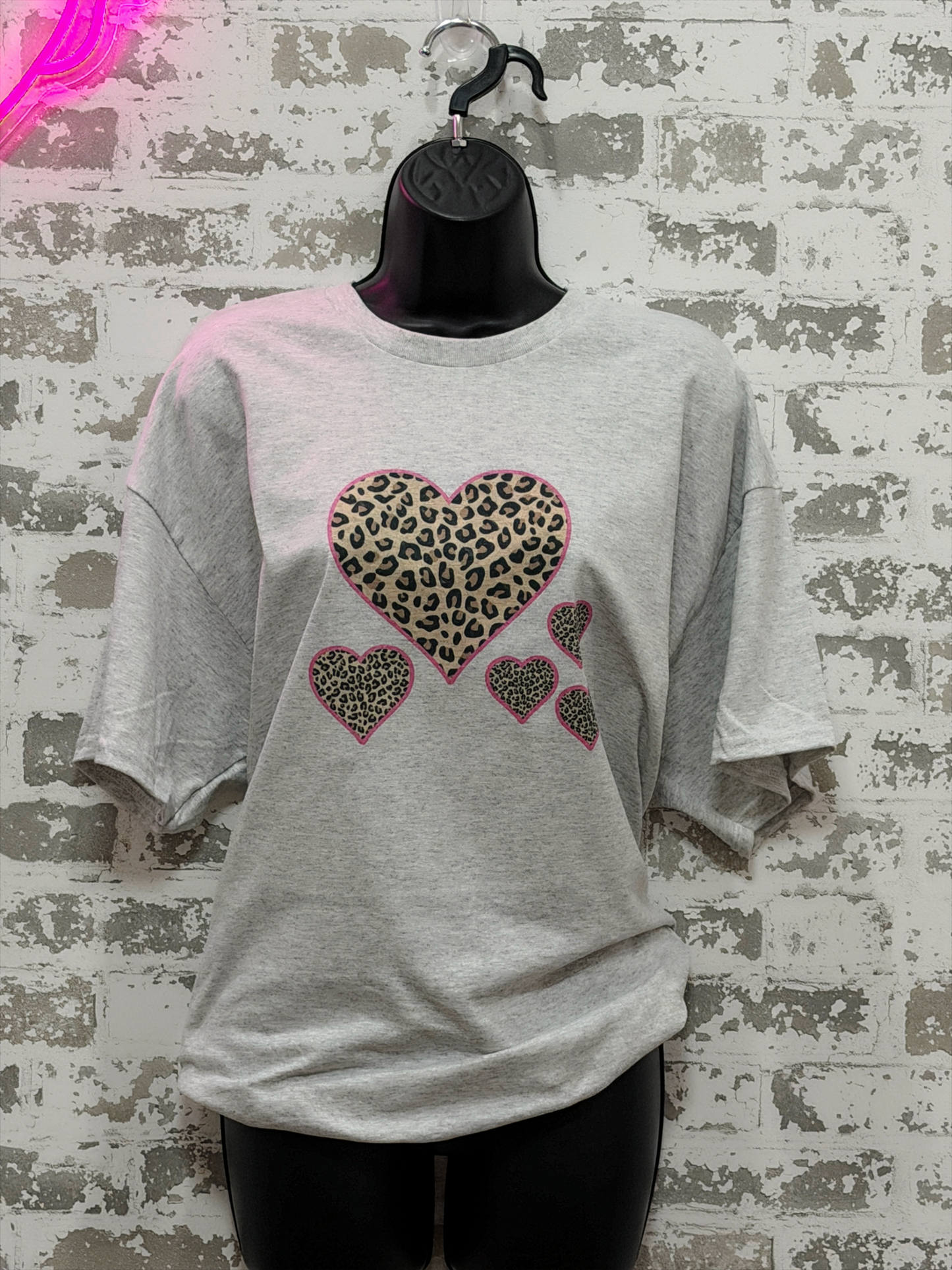 Gray t-shirt with leopard print heart designs on a textured wall background