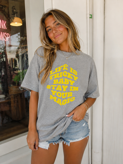 Woman wearing a gray t-shirt with yellow text standing in front of a store entrance.