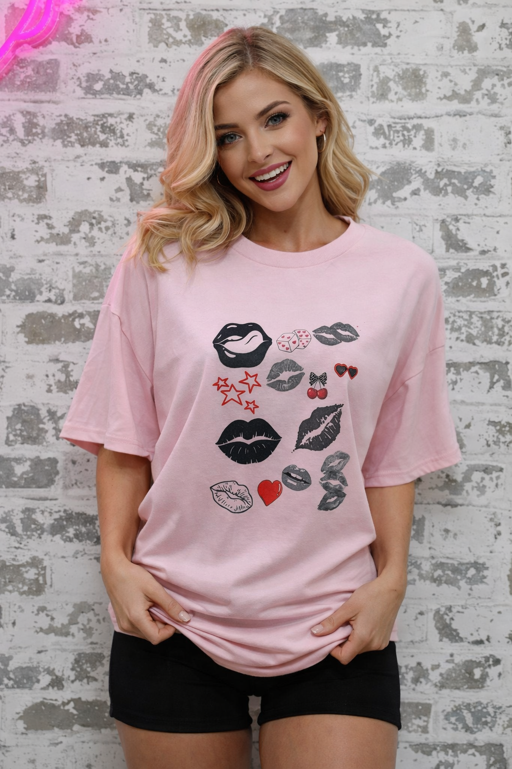 Woman wearing a pink t-shirt with graphic designs against a textured wall.