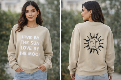 Beige sweatshirt with 'Live by the sun, love by the moon' text and sun design on a person outdoors.
